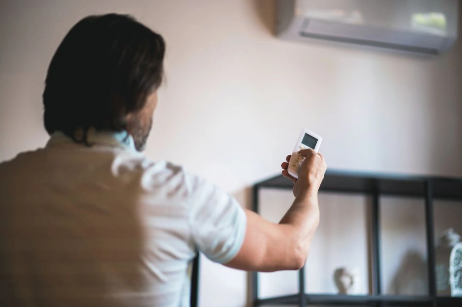 Man holding AC remote to adjust indoor air quality at home