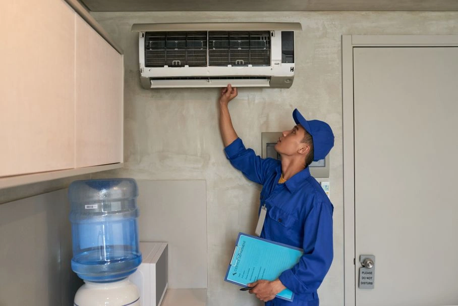 Technician checking wall-mounted AC for HVAC maintenance.